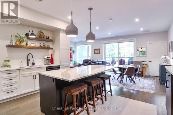 Open concept kitchen and living area with a large island, white cabinets, dark wood island base, and pendant lights. - 101 - 23 Campus Trail, Huntsville
