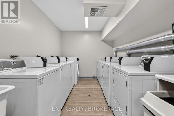 Building's shared laundry room with multiple rows of white washing machines and dryers. - 101 - 316 Kingsdale Avenue, Kingston