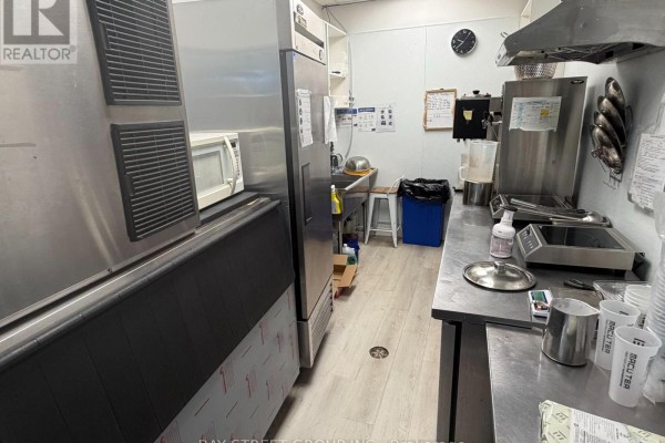 Commercial kitchen with stainless steel appliances, including a large refrigerator, microwave, and countertop equipment. - 101 - 330 Highway 7 E, Richmond Hill
