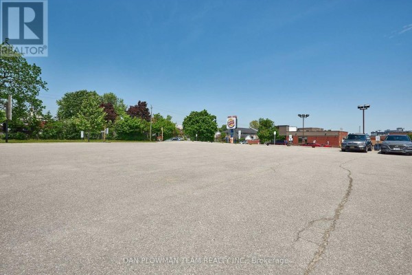 Large paved parking lot with trees and distant buildings. - 101 - 360 King Street W, Oshawa