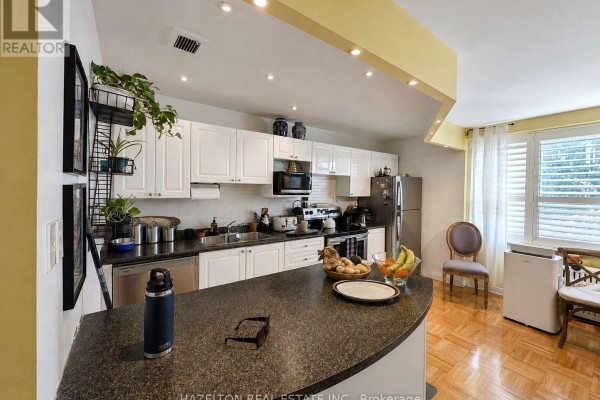Kitchen with white cabinets, stainless steel appliances, and a curved breakfast bar. - 101 - 4 Sherbourne Street N, Toronto