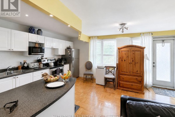 Open concept kitchen and living area with white cabinets, wood floors, and a large wardrobe. - 101 - 4 Sherbourne Street N, Toronto