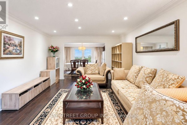 Living room with sectional sofa, wood floors, and an open doorway to a dining area. - 101 - 5 Elmira Court, Toronto