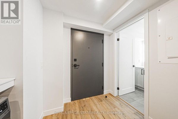 Apartment interior hallway with a grey front door, light wood floors, and a white door. - 101 - 555 Sanatorium Road, Hamilton