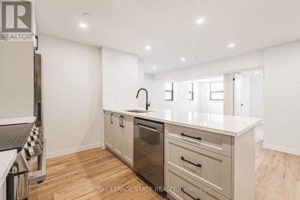 Modern apartment kitchen with light grey cabinets, white quartz countertops, and stainless steel appliances. - 101 - 555 Sanatorium Road, Hamilton