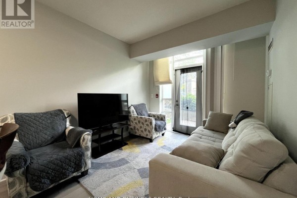 Living room seating area with large TV, two armchairs and sofa facing patio doors. - 101 - 80 Absolute Avenue, Mississauga