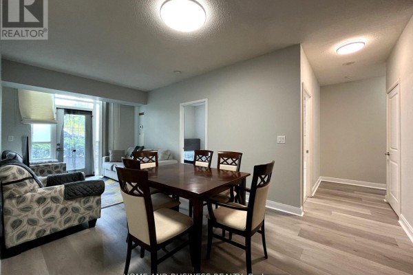 Dining area with dark wood table and chairs, adjacent to living room and hallway. - 101 - 80 Absolute Avenue, Mississauga