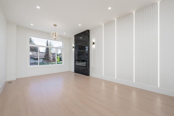 Empty living room with a black marble fireplace, white wall paneling, and large windows. - 101 14259 Park Drive, Surrey
