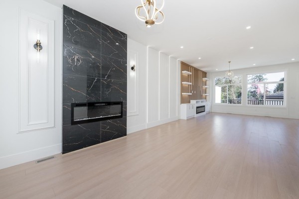 Spacious living area with a black marble fireplace, modern lighting, built-in shelving, and large windows. - 101 14259 Park Drive, Surrey