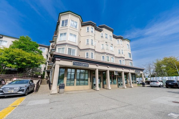 Exterior view of the apartment building showing entrance, windows, and surrounding asphalt parking lot. - 101 5765 Glover Road, Langley
