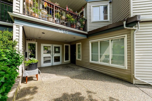 Covered entrance to the apartment building with double glass doors and potted plants. - 101 5765 Glover Road, Langley
