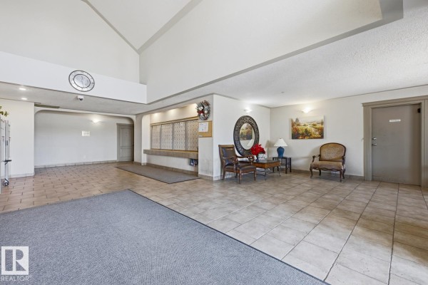 Apartment building lobby with tile flooring, mailboxes, seating area, and artwork. - #101 7511 171 St Nw, Edmonton