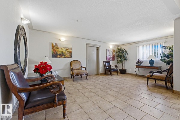 Spacious apartment building lobby with tile floors, ornate seating, artwork, and potted plants. - #101 7511 171 St Nw, Edmonton