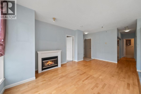 Living room with light blue walls, a white fireplace, and light wood floors. - 101 850 Royal Avenue, New Westminster