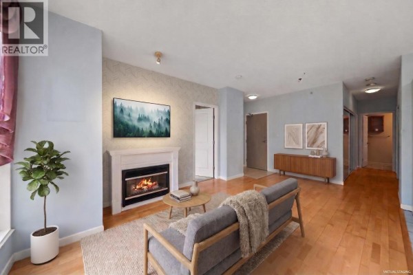 Staged living room with a sofa, coffee table, fireplace, and wall art. - 101 850 Royal Avenue, New Westminster