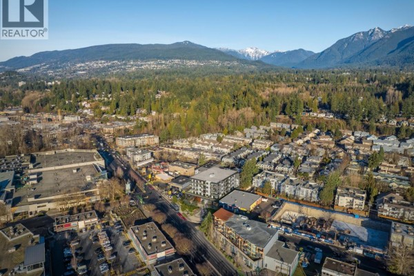 Aerial view of a North Vancouver neighborhood with a mixed-use building surrounded by residential areas and mountains. - 101 880 W 15th Street, North Vancouver