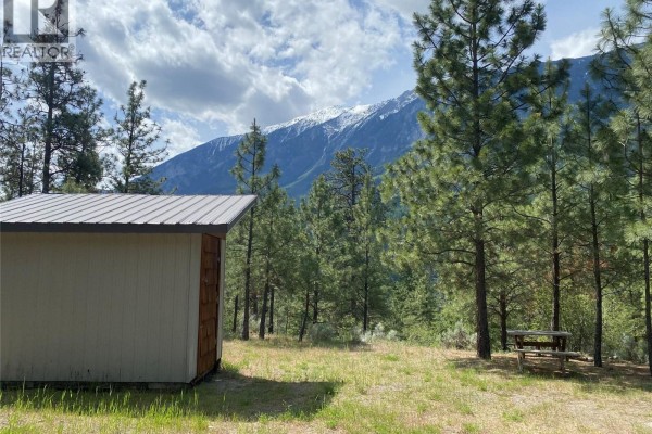 Small shed with beige siding and metal roof next to pine trees and distant mountains. - 101 Airport Road, Lillooet
