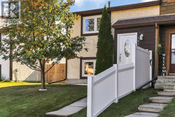 Front exterior of a townhouse with a white picket fence and green lawn. - 101 Baile Close, Red Deer