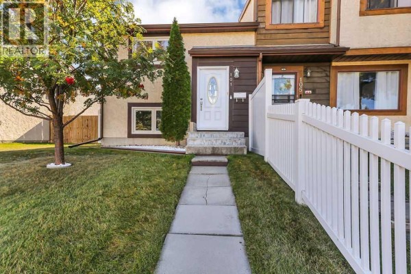 Pathway leading to the front door of a townhouse with a white picket fence. - 101 Baile Close, Red Deer
