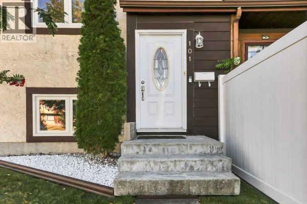 Close-up of the front door of a townhouse with concrete steps and a white fence. - 101 Baile Close, Red Deer