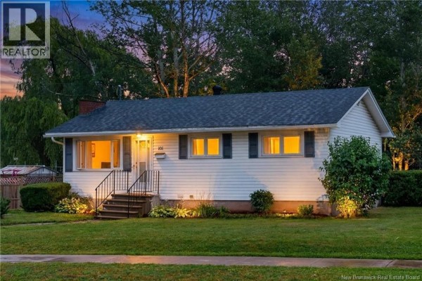 Front exterior of the white bungalow at dusk, illuminated by exterior lights. - 101 Birchmount Drive, Moncton