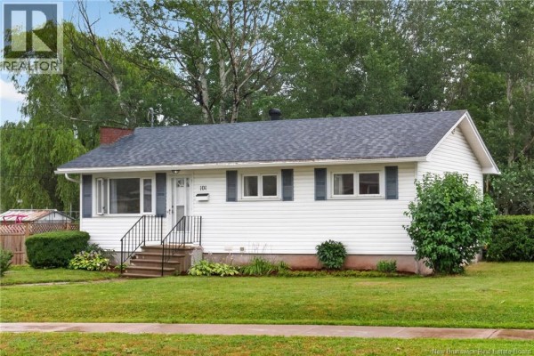Side exterior view of the white bungalow with green lawn and mature trees. - 101 Birchmount Drive, Moncton