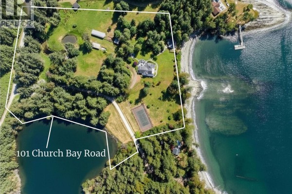 Living room with wood floor, large sliding glass doors opening to a deck and water view. - 101 Church Bay Rd, Saturna Island