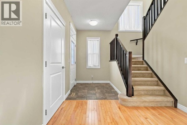 Interior entryway with hardwood floors, tiled floor, white doors, and staircase with dark banister. - 101 Cimarron Vista Crescent, Okotoks