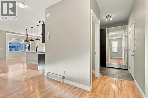 Open concept living area with hardwood floors, kitchen island, pendant lights, and large window. - 101 Cimarron Vista Crescent, Okotoks