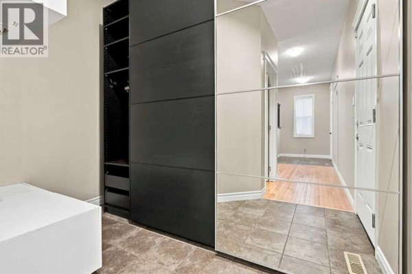 Hallway with tiled floor, mirrored closet doors, white doors, and view into another room. - 101 Cimarron Vista Crescent, Okotoks
