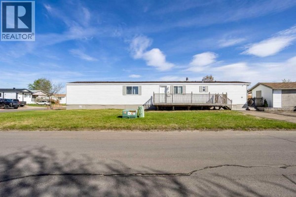 Front exterior of a white mobile home with a wooden deck covered in snow. - 101 Clausen Crescent, Fort Mcmurray