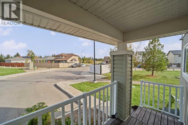 View from a covered front porch overlooking a paved street and neighboring houses. - 101 Clover Way, Carstairs