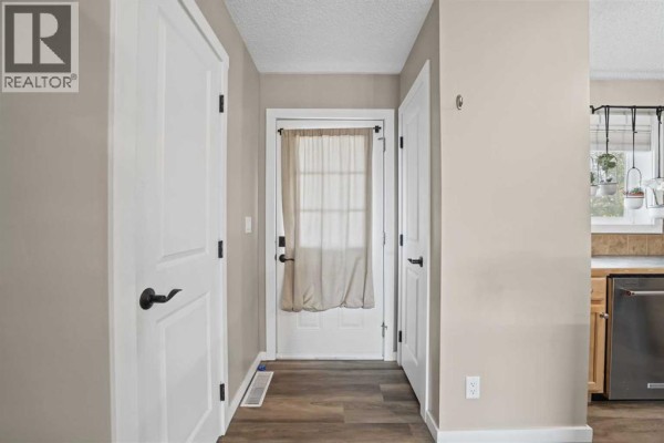 Interior hallway with beige walls, white doors, wood-look flooring, and a back door. - 101 Clover Way, Carstairs