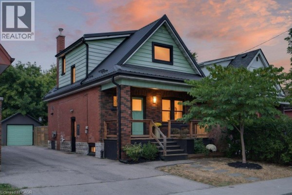 Exterior view of a two-story red brick house with green siding and a black metal roof at dusk. - 101 Cope Street, Hamilton