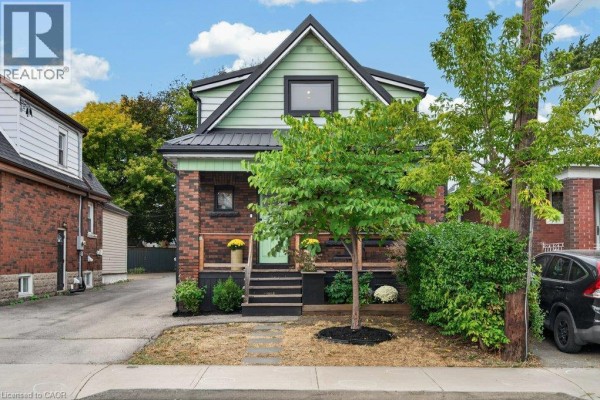 Front view of a red brick house with green trim, a small tree, and lush landscaping on a sunny day. - 101 Cope Street, Hamilton