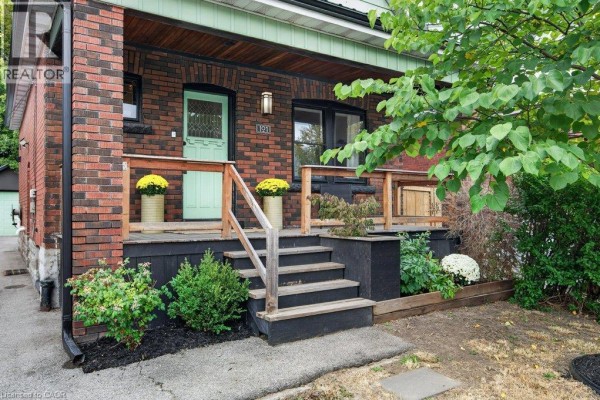 Close-up of the front porch with wooden railings, stairs, green door, and potted yellow flowers. - 101 Cope Street, Hamilton