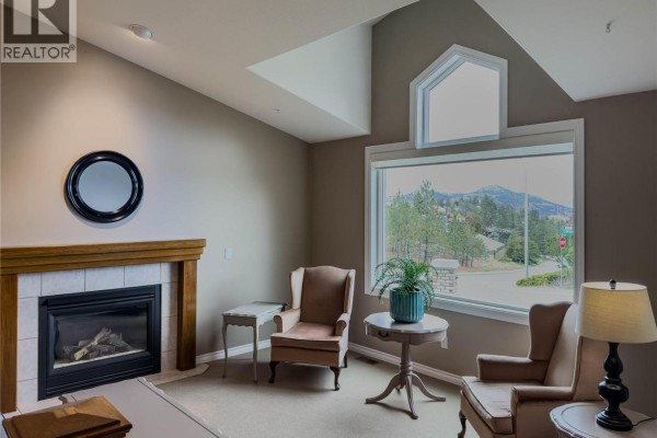 Living room with a gas fireplace, two armchairs, and a large window overlooking the street. - 101 Coppertree Court, Kamloops