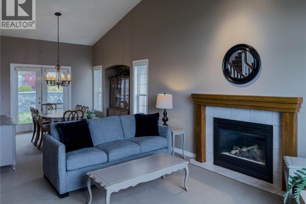 Living room with a grey sofa, coffee table, gas fireplace, and dining area visible. - 101 Coppertree Court, Kamloops