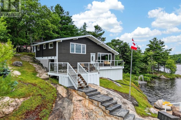 Side view of the waterfront home with a Canadian flag, surrounded by trees and overlooking the lake. - 101 Healey Lake Water, The Archipelago