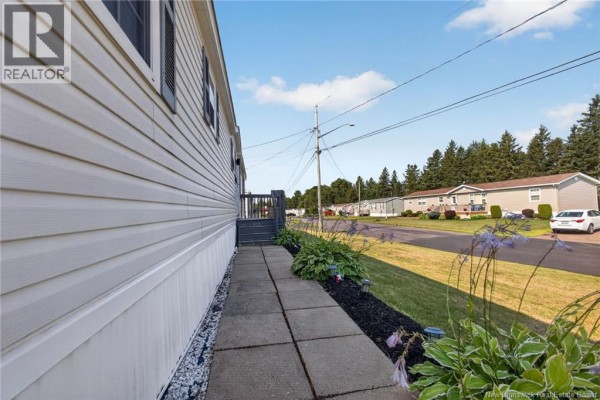 Concrete walkway beside the home with green landscaping and a view of the street. - 101 Nepisiguit, Dieppe