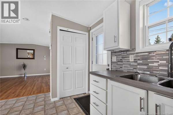 Kitchen view showing white cabinets, stainless steel sink, and doorway to living room. - 101 Nepisiguit, Dieppe