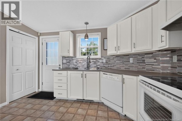 Kitchen with white cabinets, grey backsplash, sink, dishwasher, and oven against a window. - 101 Nepisiguit, Dieppe