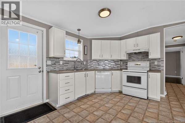 Corner view of the kitchen showing white cabinets, sink, dishwasher, oven, and doorway. - 101 Nepisiguit, Dieppe