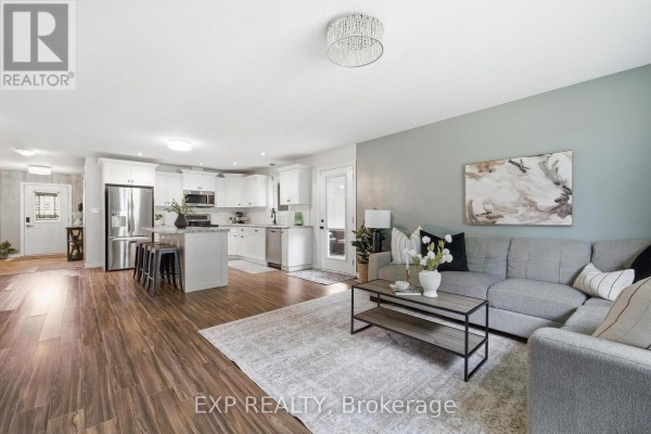 Open concept living room and kitchen with a grey sectional sofa and white cabinets. - 101 Tuffy Macdougall Court, Minto