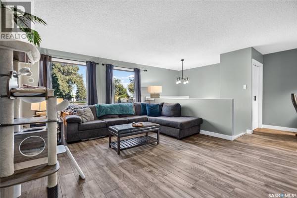 Living room with grey sectional sofa, coffee table, and large windows with dark blue curtains. - 1010 9th Avenue Sw, Moose Jaw
