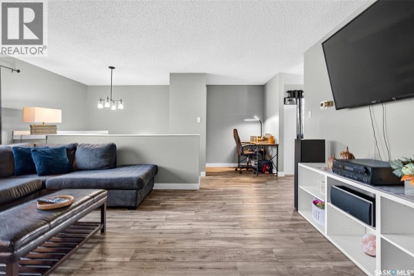 Living room with grey sectional sofa, coffee table, cat tree, and view of outside through windows. - 1010 9th Avenue Sw, Moose Jaw