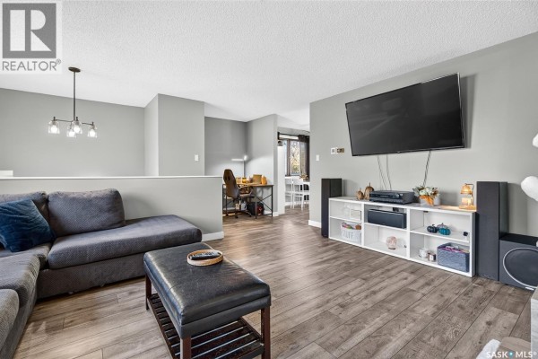 Living room with sectional sofa, TV on wall, entertainment unit, and a desk area in the background. - 1010 9th Avenue Sw, Moose Jaw