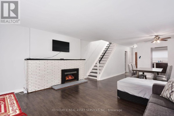 Living room with dark wood floors, a white brick fireplace, a TV, and a staircase. - 1010 Kipps Lane, London East