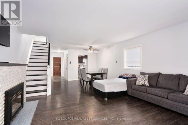 Living room with a sofa, dining table, dark wood floors, and a white brick fireplace. - 1010 Kipps Lane, London East