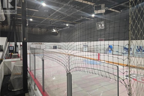 Indoor ice rink viewed through safety netting, showing advertising boards on the side walls. - 1010 Lorne Street Unit# 115, Sudbury